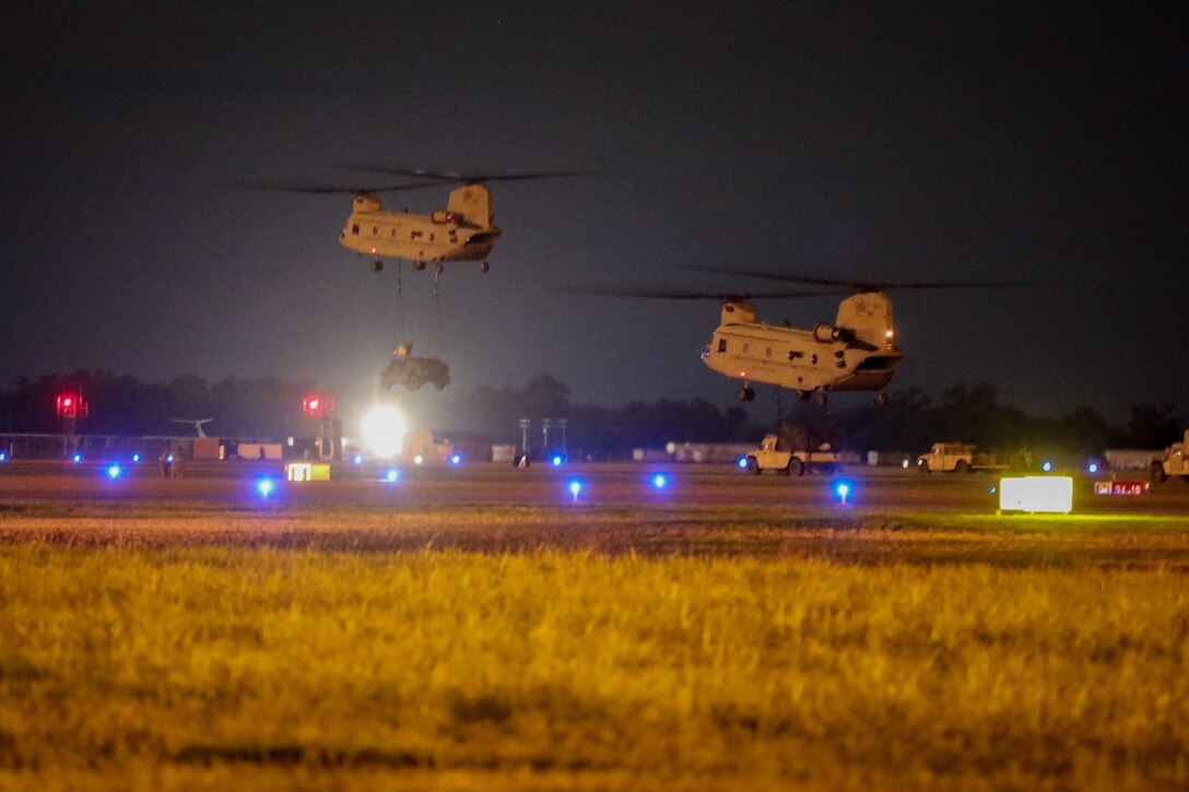 Two helicopters fly together at night.