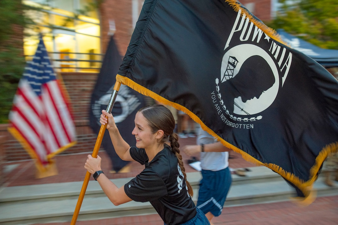 A cadet runs with a POW/MIA flag.