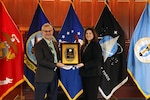 man and woman holding award with service flags in background