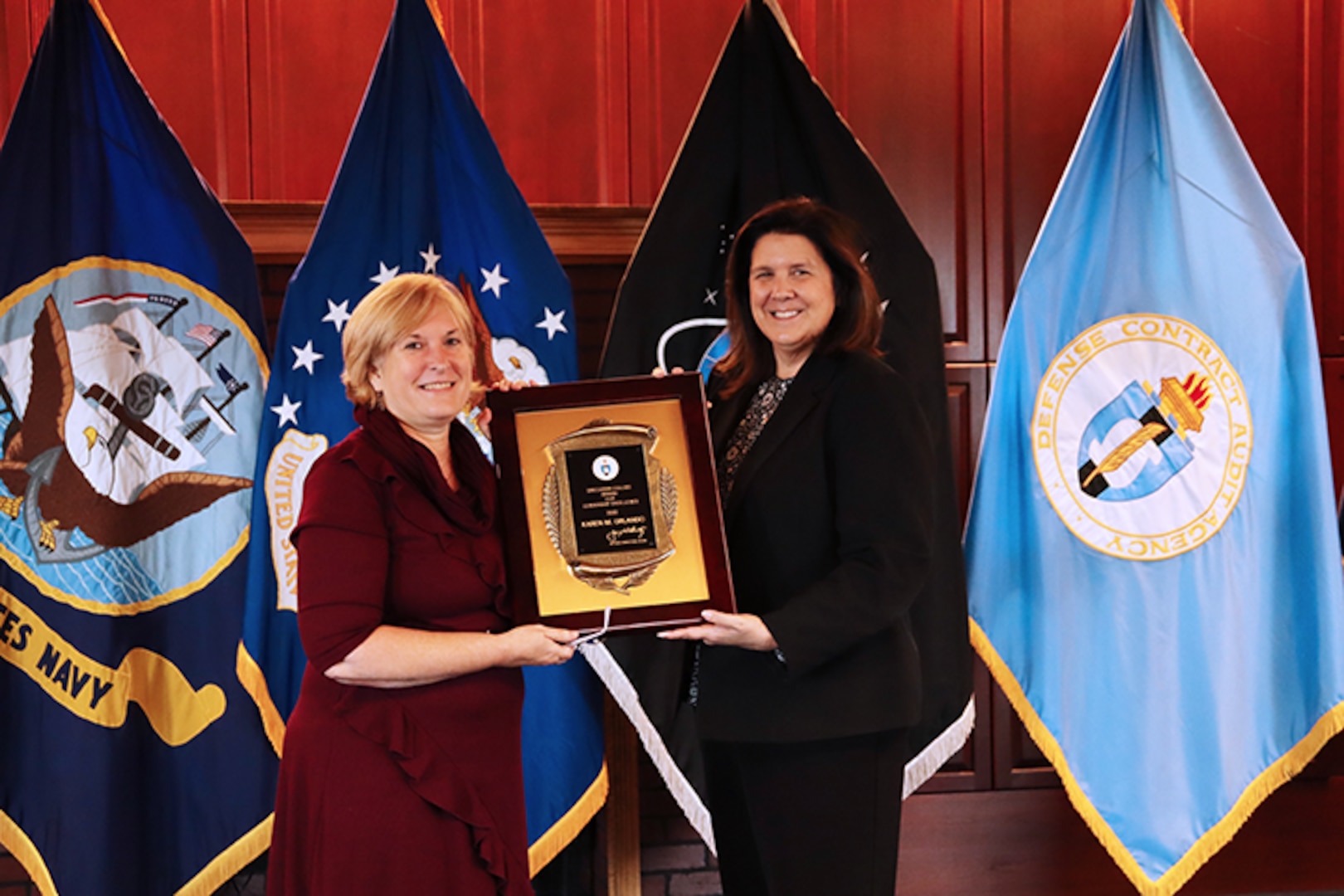 two women holding award in front of service flags