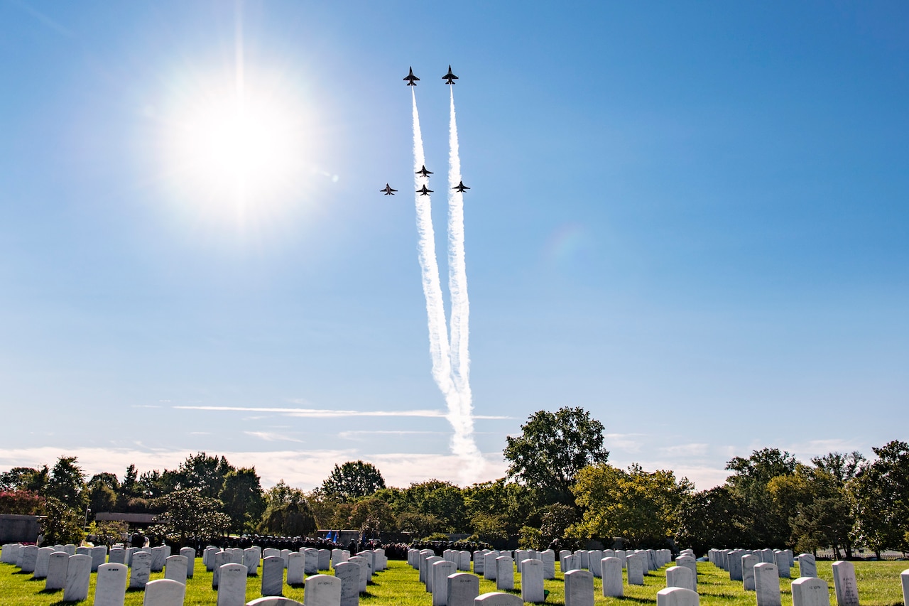Aircraft fly over a cemetery during a funeral service.