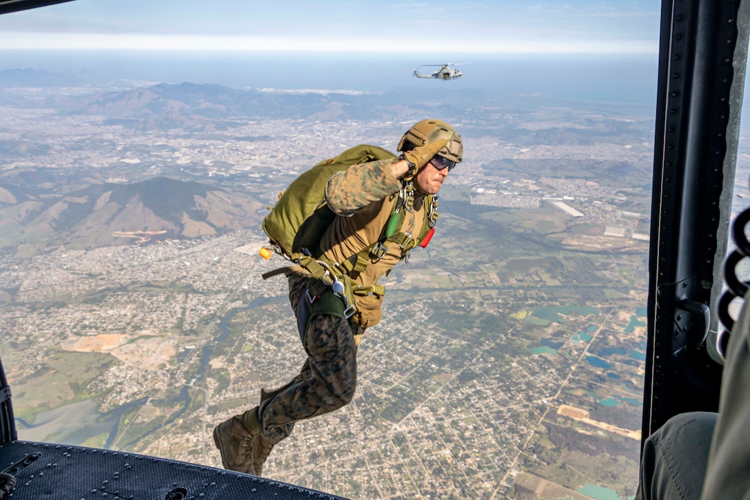 A Marine salutes while jumping out of an airborne helicopter.