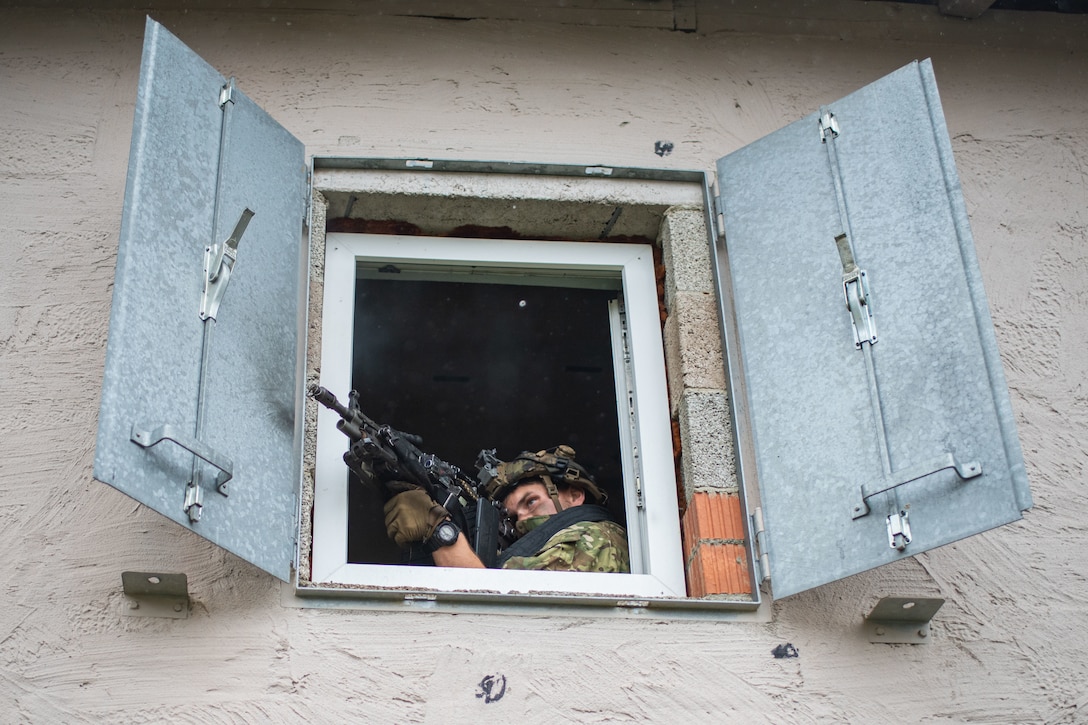 A paratrooper aims his weapon from a window.