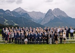 About 100 people in business attire pose for a group photo with tall mountains behind them