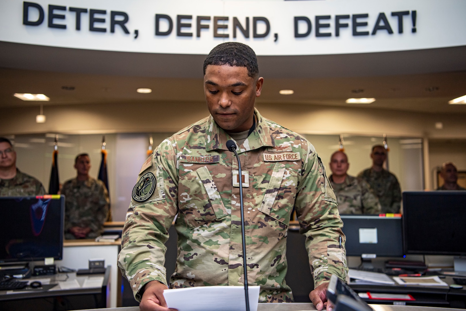 Military man in uniform speaking into microphone, reading from a piece of paper