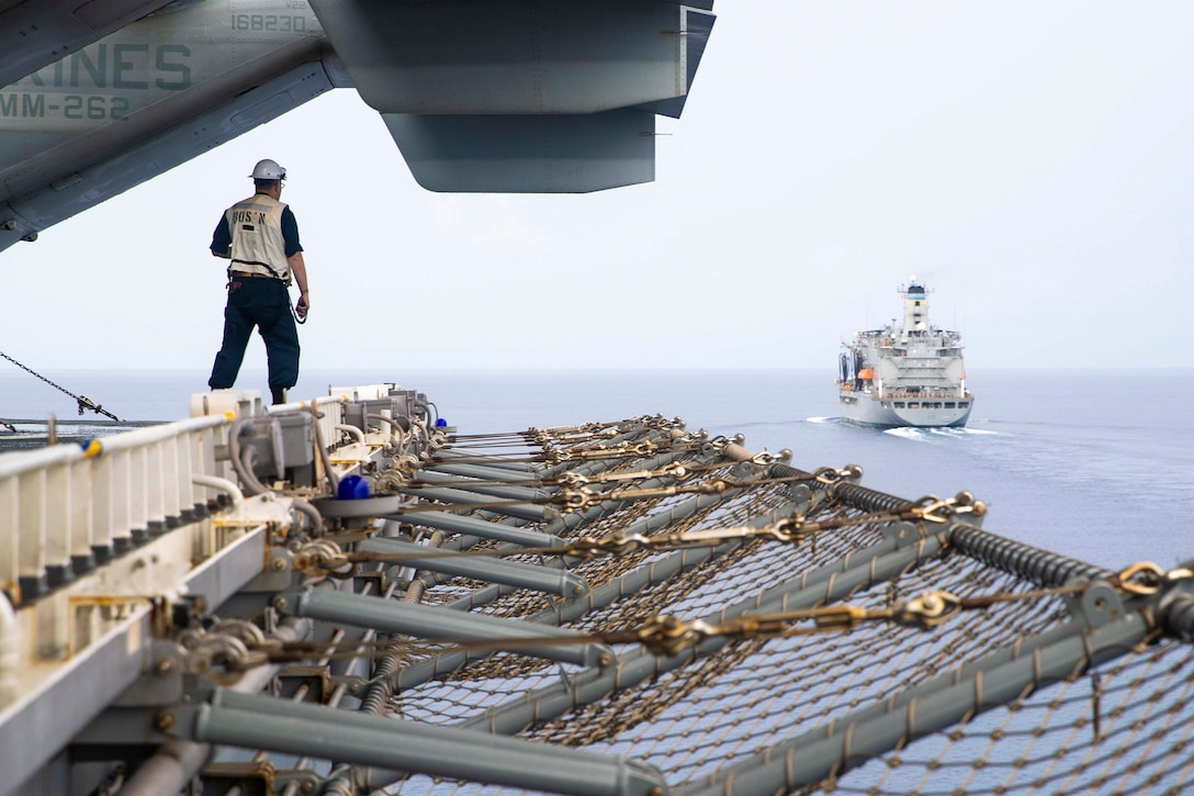 A sailor watches a ship travel through waters while standing aboard another ship.