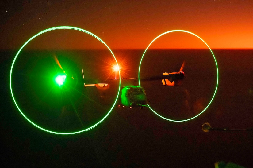Lights shine around an airborne helicopter at night.