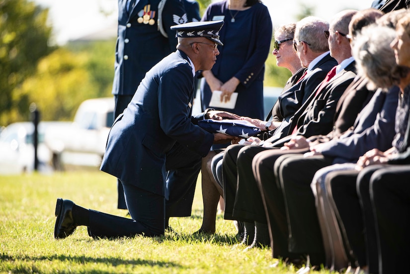 Chief of Staff of the U.S. Air Force Gen. Charles Q. Brown, Jr. presents to U.S. flag to one of several attendees seated in a cemetery.