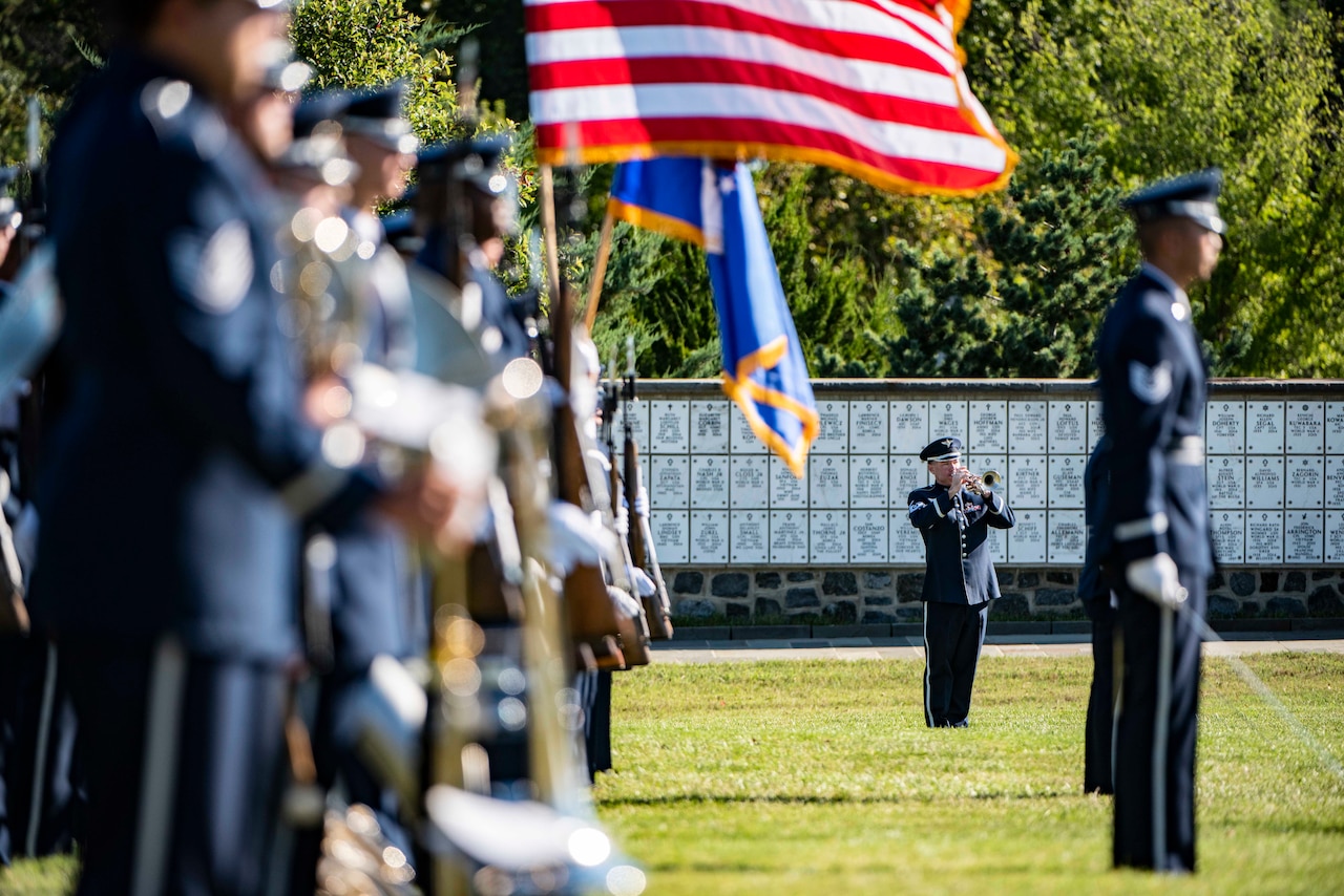 A trumpeter performs in a cemetery while service members stand, some holding flags.