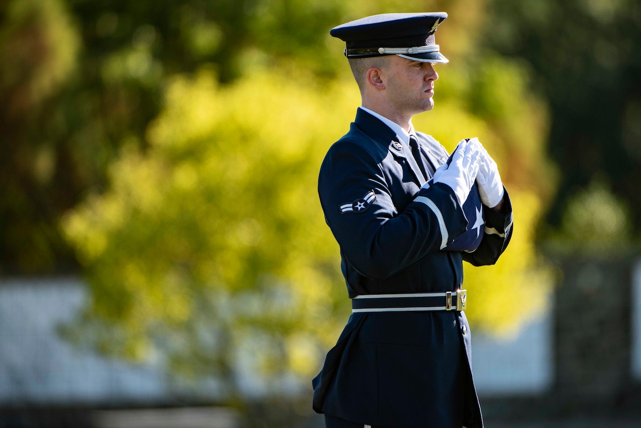 A service member stands holding a folded flag to the chest.