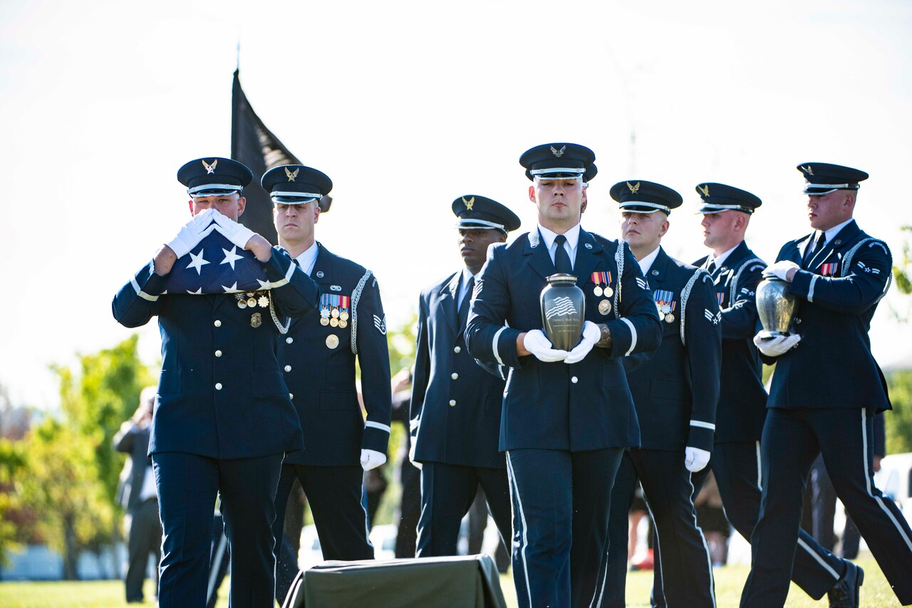 Airmen walk in formation carrying a flag and urn.