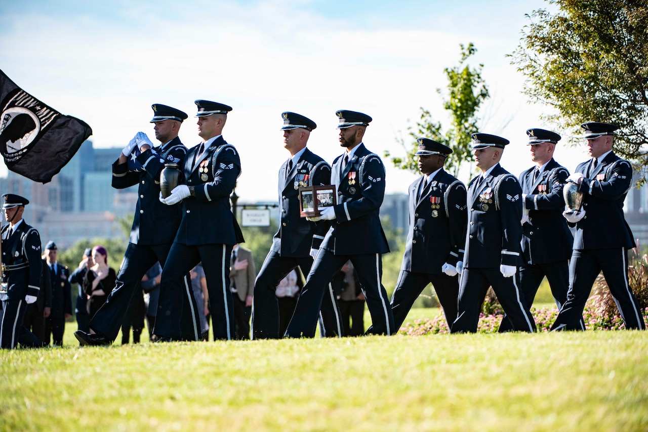 Airmen walk in formation carrying a flag and urn.