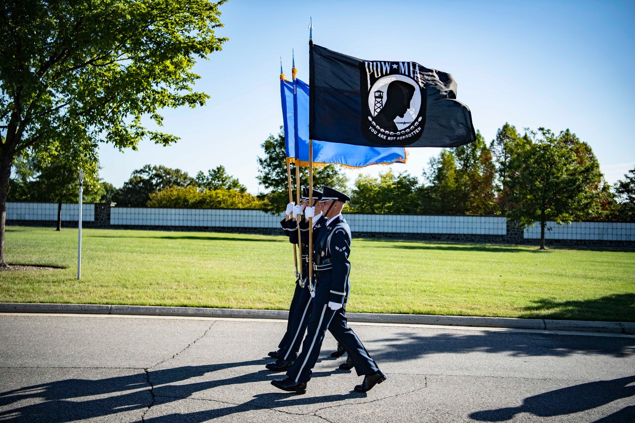 Service members carry flags along a road in a cemetery.