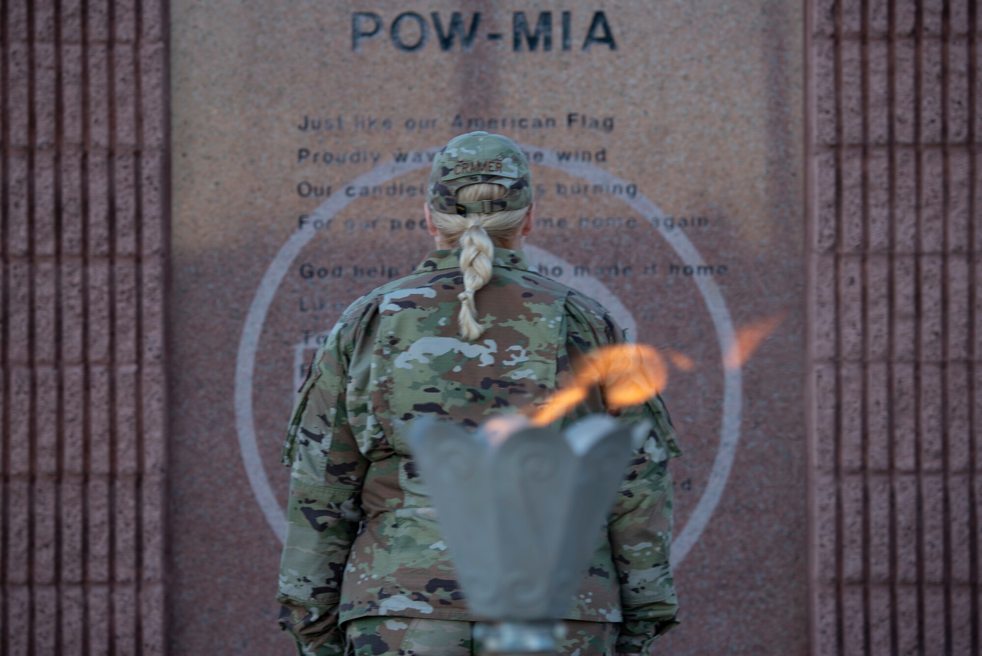 A woman in green occupational camouflaged pattern uniform stands in front of a POW/MIA memorial.