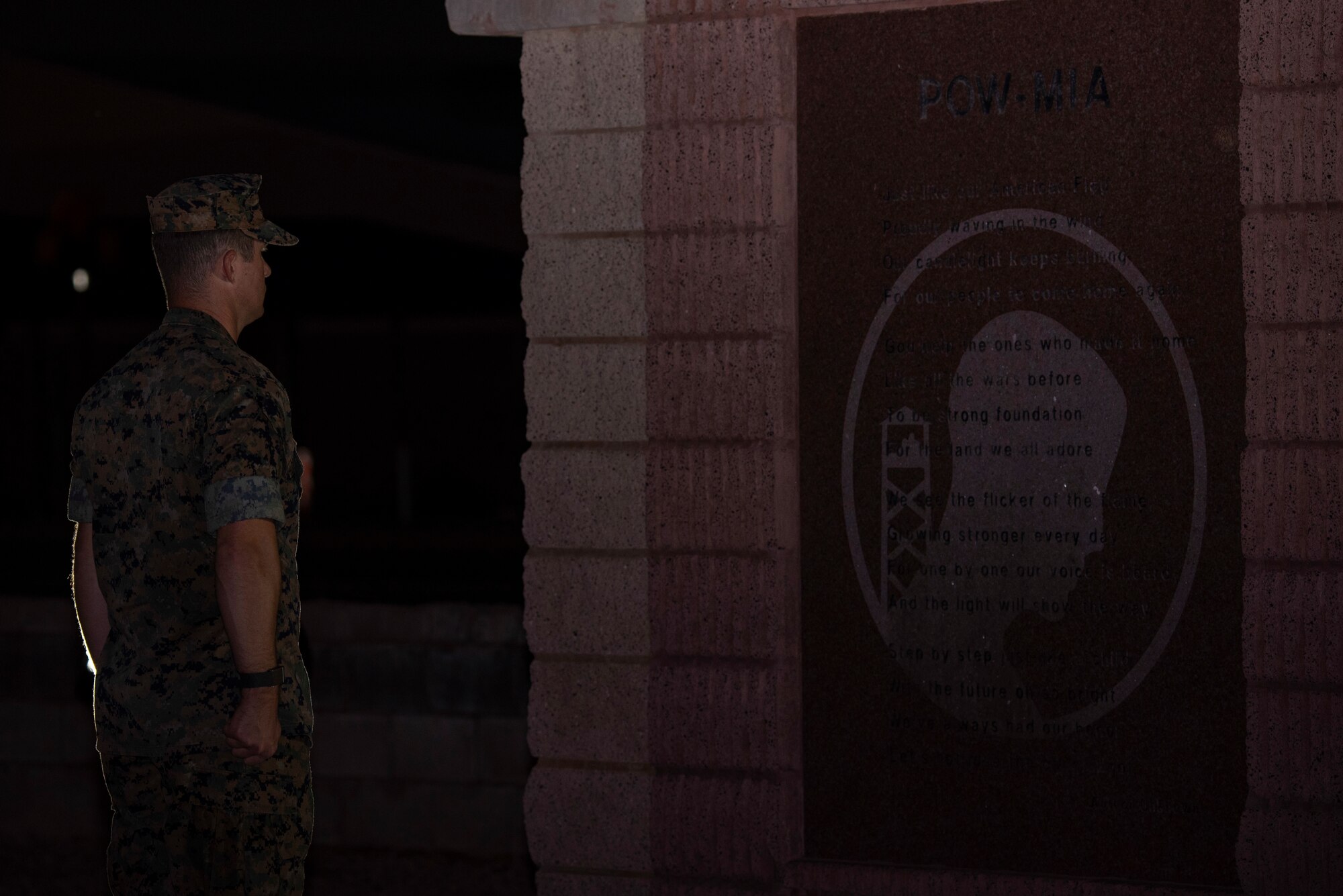 A man in Marine Corps uniform stands in front of a POW/MIA memorial.