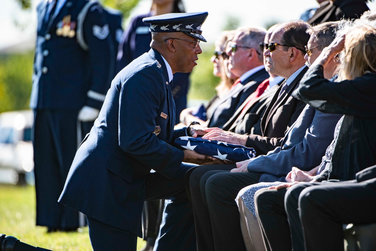 Chief of Staff of the U.S. Air Force Gen. Charles Q. Brown, Jr. presents a folded flag to one of several people seated in a cemetery.