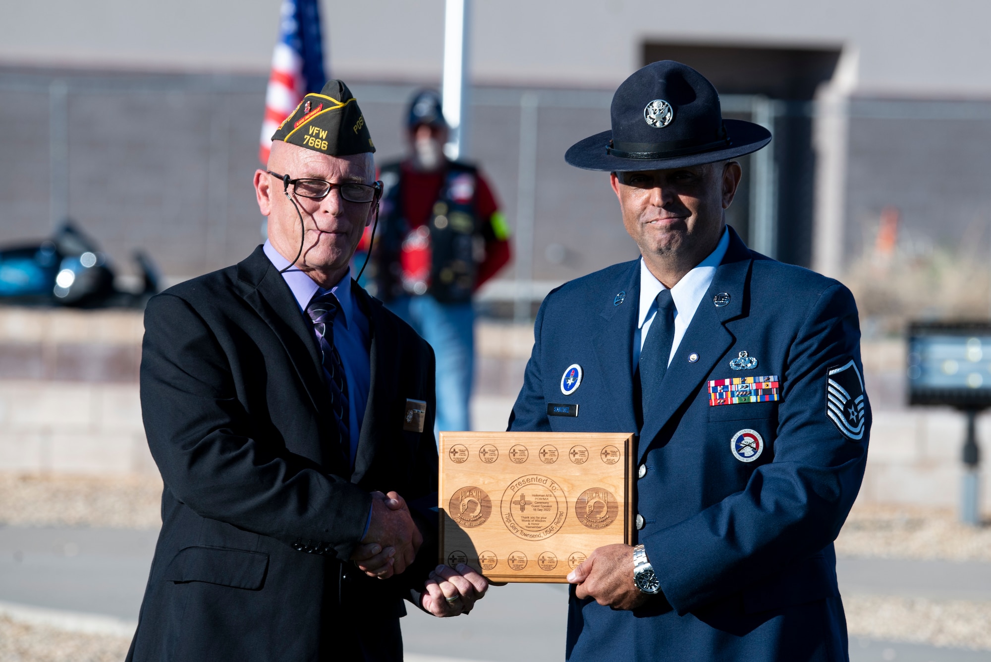 A man in a suit accepts a plaque from a man in Air Force dress blues.