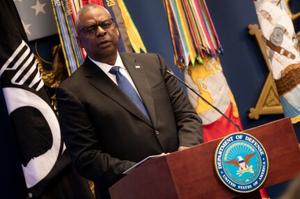 A man wearing business attire stands behind a lectern with a microphone.