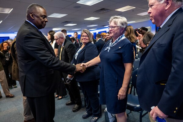 The Secretary of Defense shakes hands with a woman in a crowd.