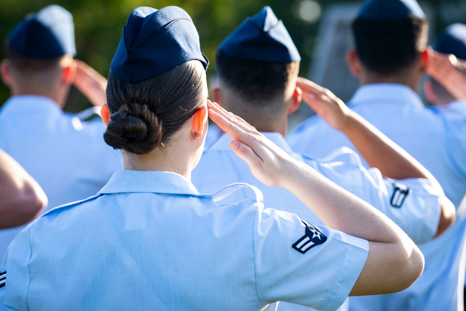 Airmen, shown from behind, stand outside in formation and salute.