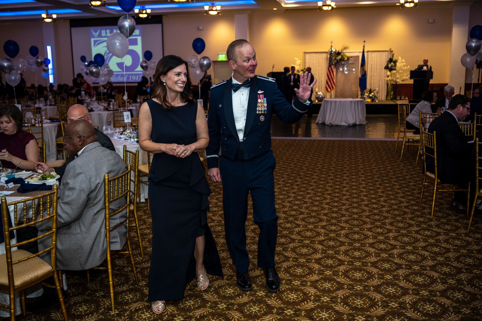 A man and woman in very nice clothes wave.