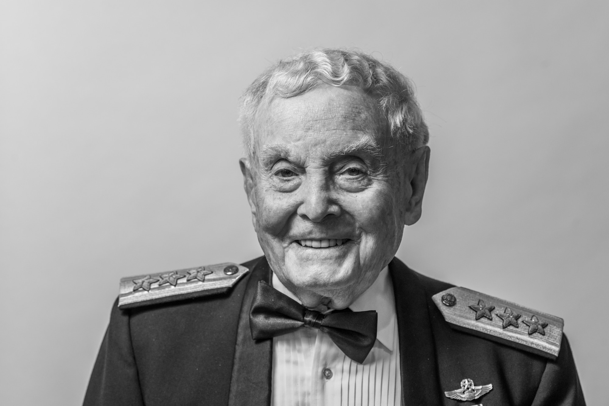 A man wearing a ceremonial dress uniform stands in front of a white background.