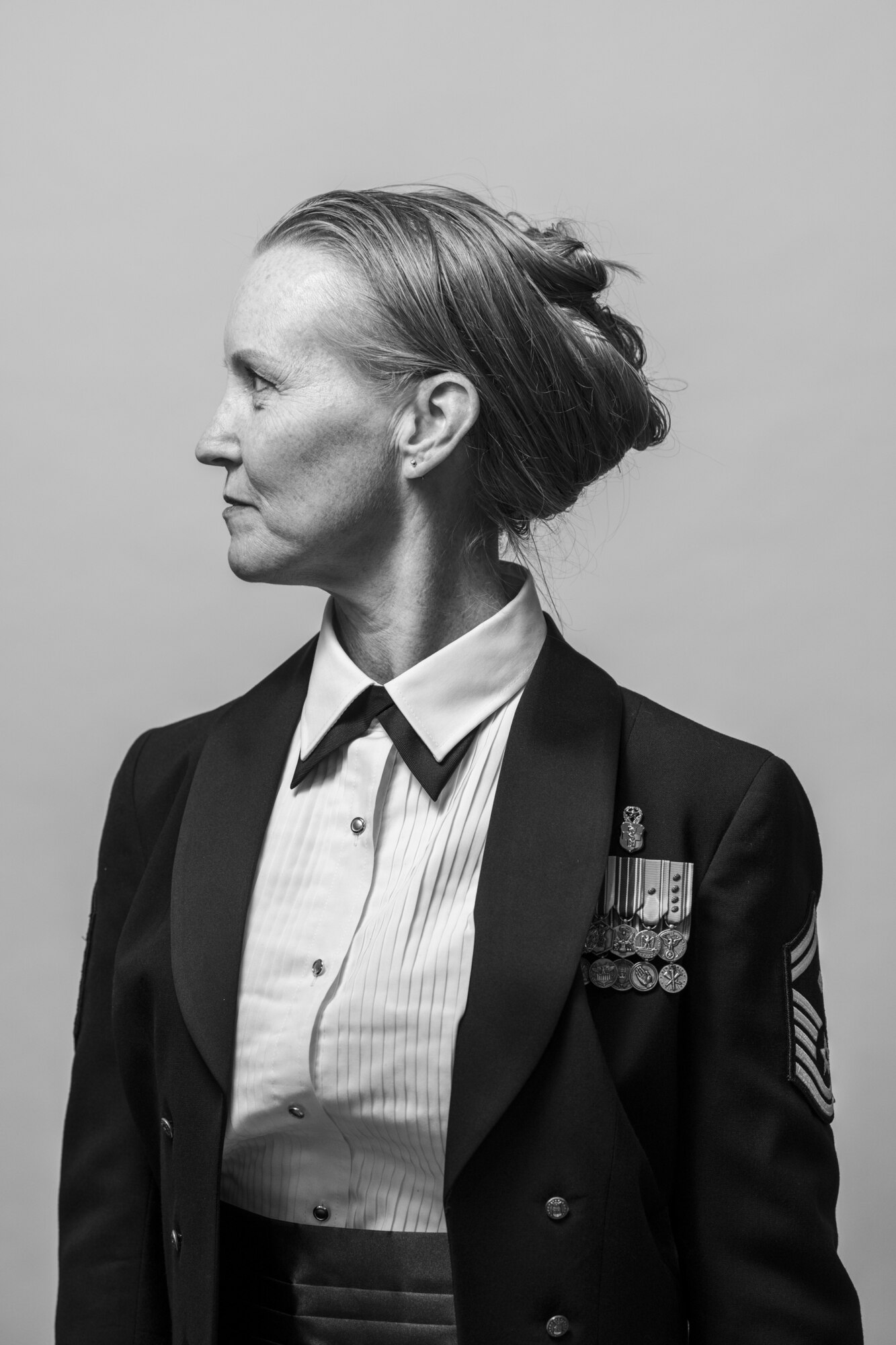 A woman stands in front of a white background wearing a dress uniform.