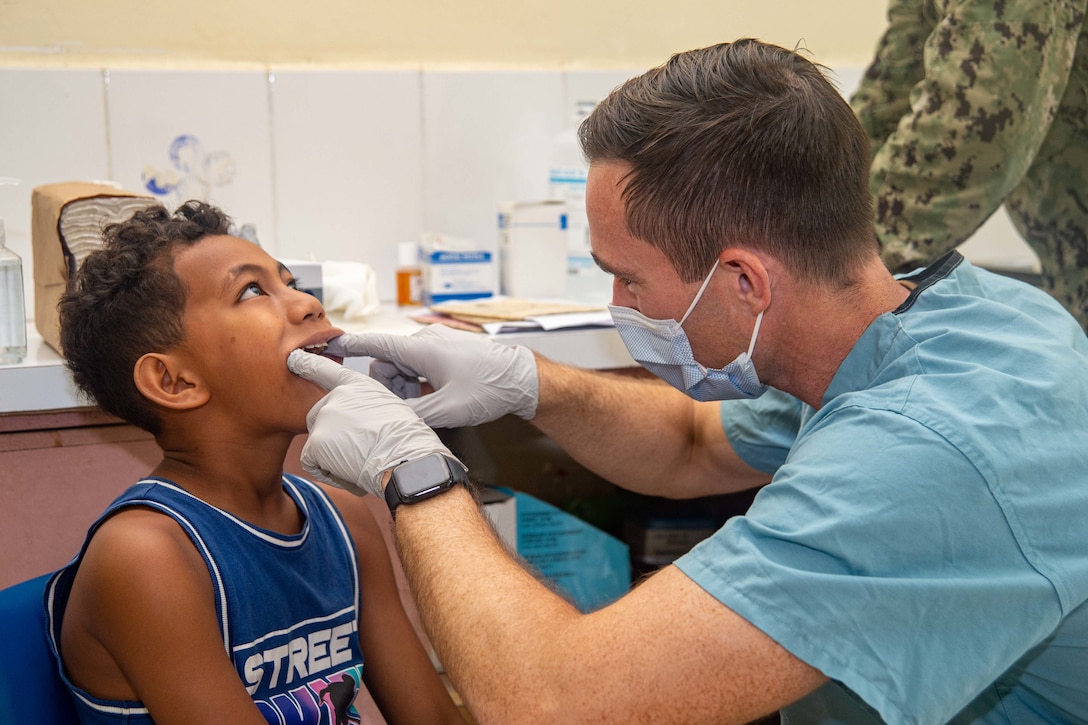 A Navy officer conducts a dental exam on a young boy.