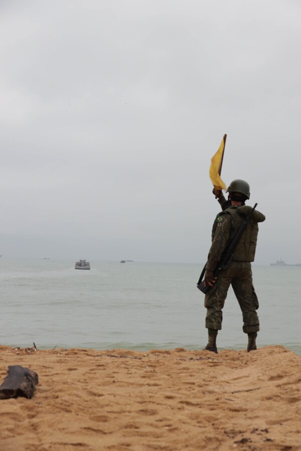 A Brazilian Marine waves a flag to signal the clearance of the beachhead during an amphibious landing as part of exercise UNITAS LXIII in Itaoca, Brazil, Sept. 16, 2022. UNITAS is the world’s longest-running annual multinational maritime exercise that focuses on enhancing interoperability among multiple nations and joint forces during littoral and amphibious operations in order to build on existing regional partnerships and create new enduring relationships that promote peace, stability, and prosperity in the U.S. Southern Command’s area of responsibility. (U.S. Marine Corps photo by Lance Cpl. Trystan Taft)