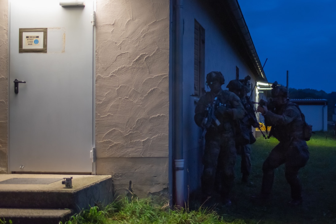 Armed soldiers take position on the side of a building at night.