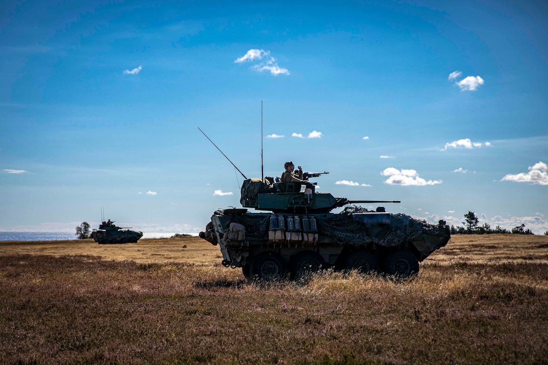 Service members operate two tanks driving through a field.