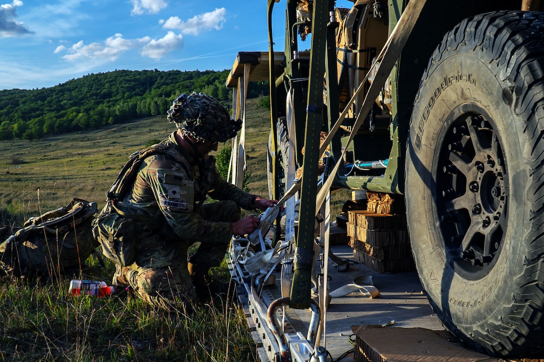 A soldier uses straps to secure a vehicle to a pallet in a field environment.
