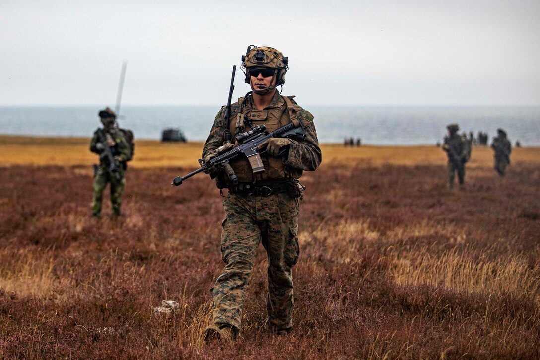 An armed Marine walks through a field.