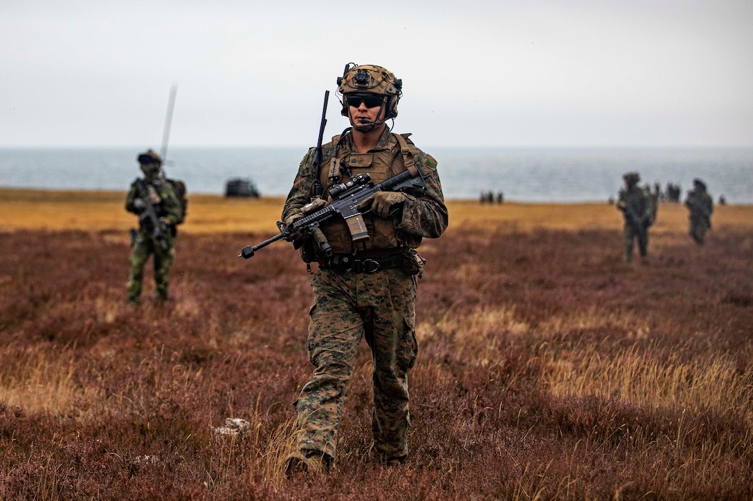 An armed Marine walks through a field.