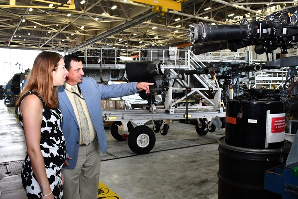 Man points at H-53 rotor head as female government official looks on