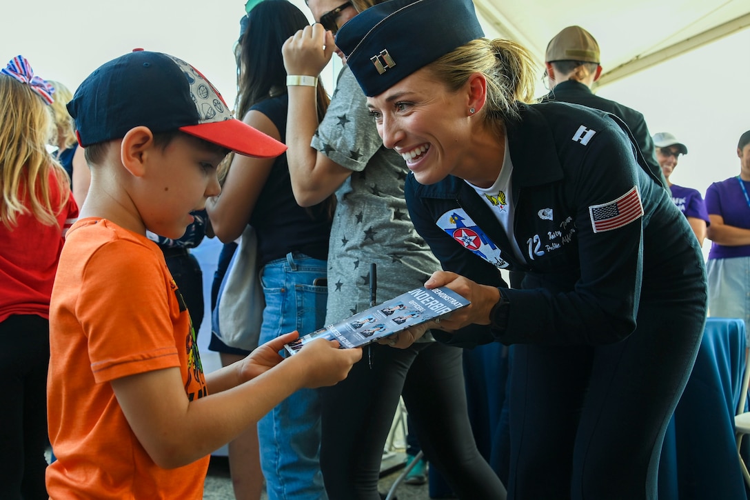 An airman smiles at a child while showing him a pamphlet.