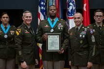 three people wearing U.S. army uniforms posed on a stage accepting awards.