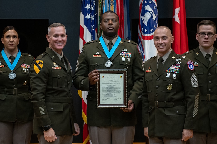 three people wearing U.S. army uniforms posed on a stage accepting awards.