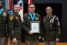 three people wearing U.S. army uniforms posed on a stage accepting awards.