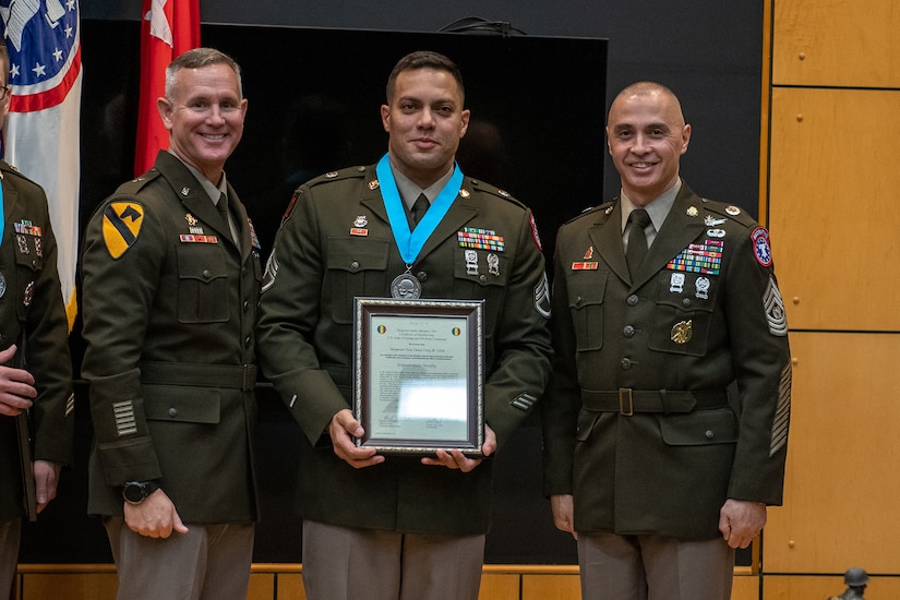 three people wearing U.S. army uniforms posed on a stage accepting awards.