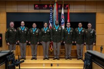 three people wearing U.S. army uniforms posed on a stage accepting awards.