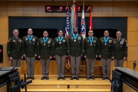 three people wearing U.S. army uniforms posed on a stage accepting awards.