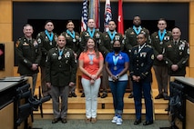 three people wearing U.S. army uniforms posed on a stage accepting awards.