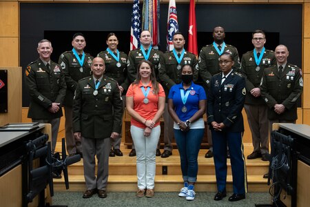 three people wearing U.S. army uniforms posed on a stage accepting awards.