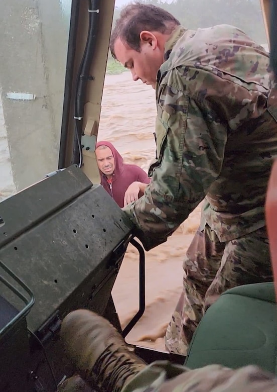 A service member leans out of a vehicle to help a civilian caught up in floodwaters.