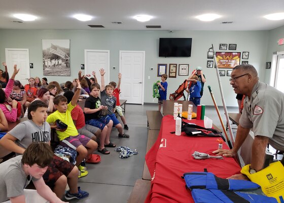 Campers enthusiastically raise their hands volunteering to try on variously sized lifejackets from Park Ranger Bobby Bartlett’s water safety table, during water safety class at Dale Hollow Lake Trooper Island in Burkesville, Kentucky.