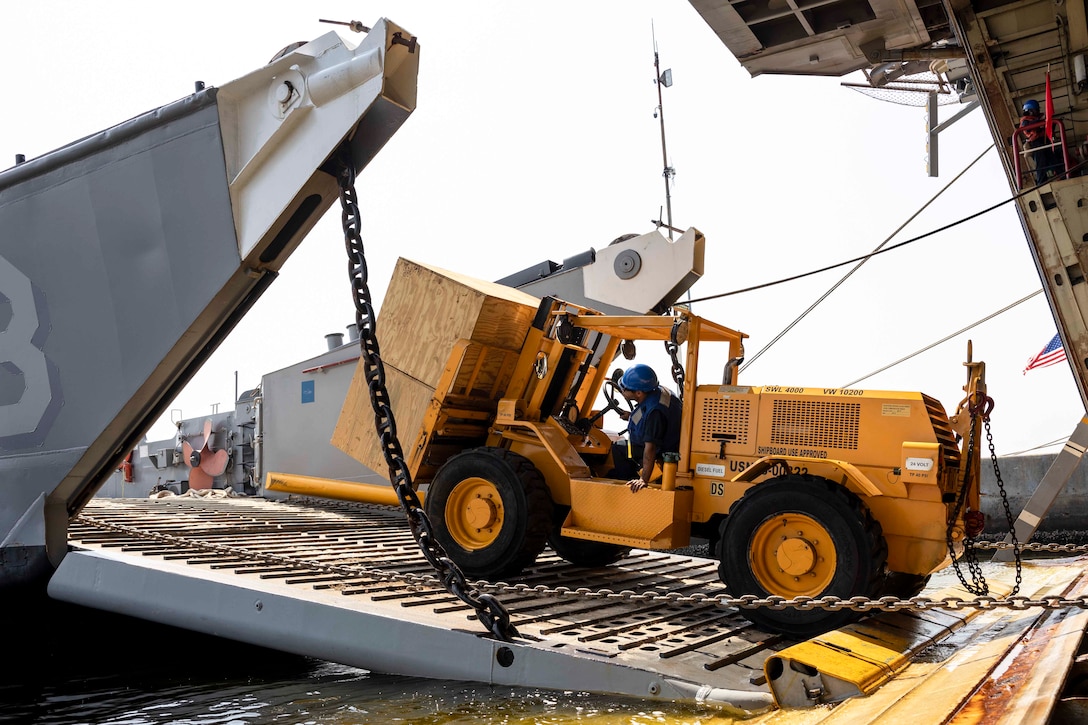 A sailor drives a forklift to move equipment onto an air-cushioned landing craft.