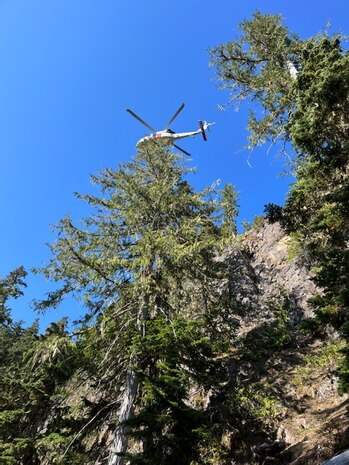 A Search and Rescue (SAR) helicopter from Naval Air Station (NAS) Whidbey Island hovers above during a rescue of a stranded hunter trapped on a cliff face near Mt. Constance in the Olympic National Forest on Sept. 18, 2022.