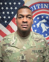 man wearing u.s. army uniform standing in front of flags.