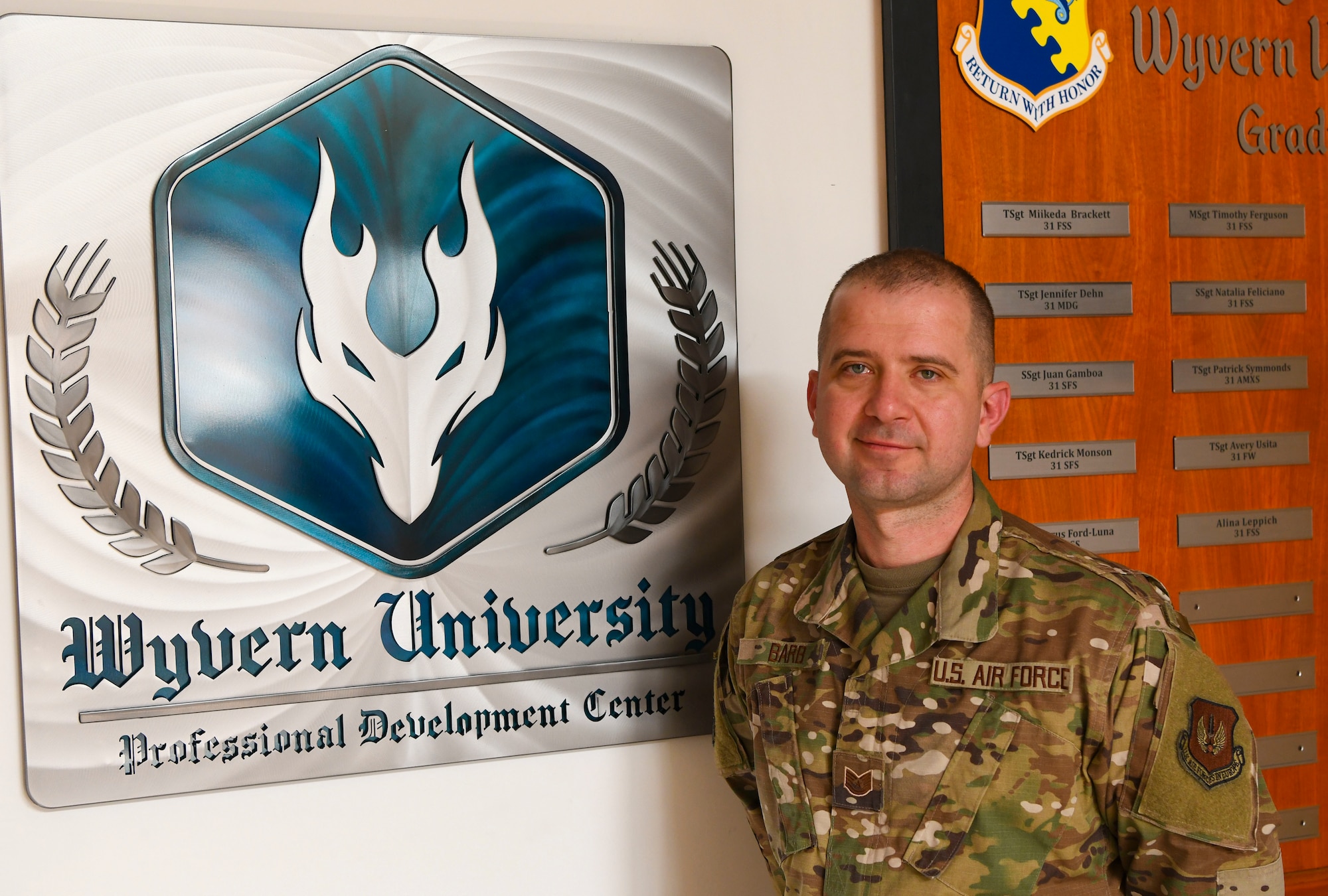 Tech. Sgt. Adam Barb, 31st Force Support Squadron NCOIC of professional development, stands in front of Wyvern University (WU) Graduate plaque.